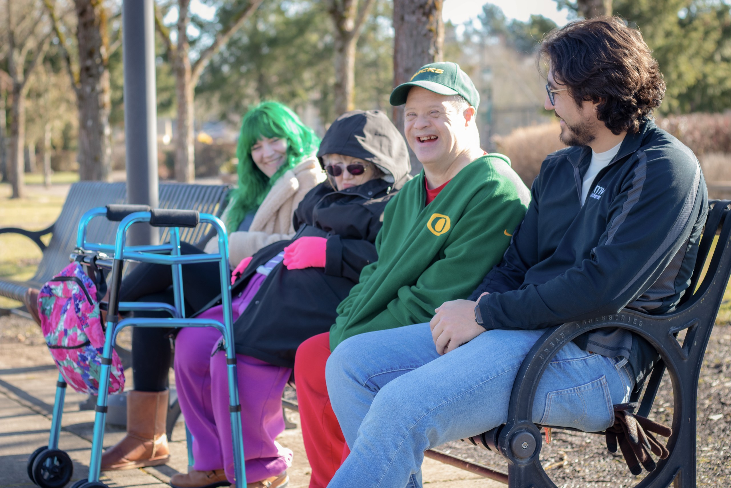 MVA Volunteers sit with people they are serving on a park bench, smiling and chatting