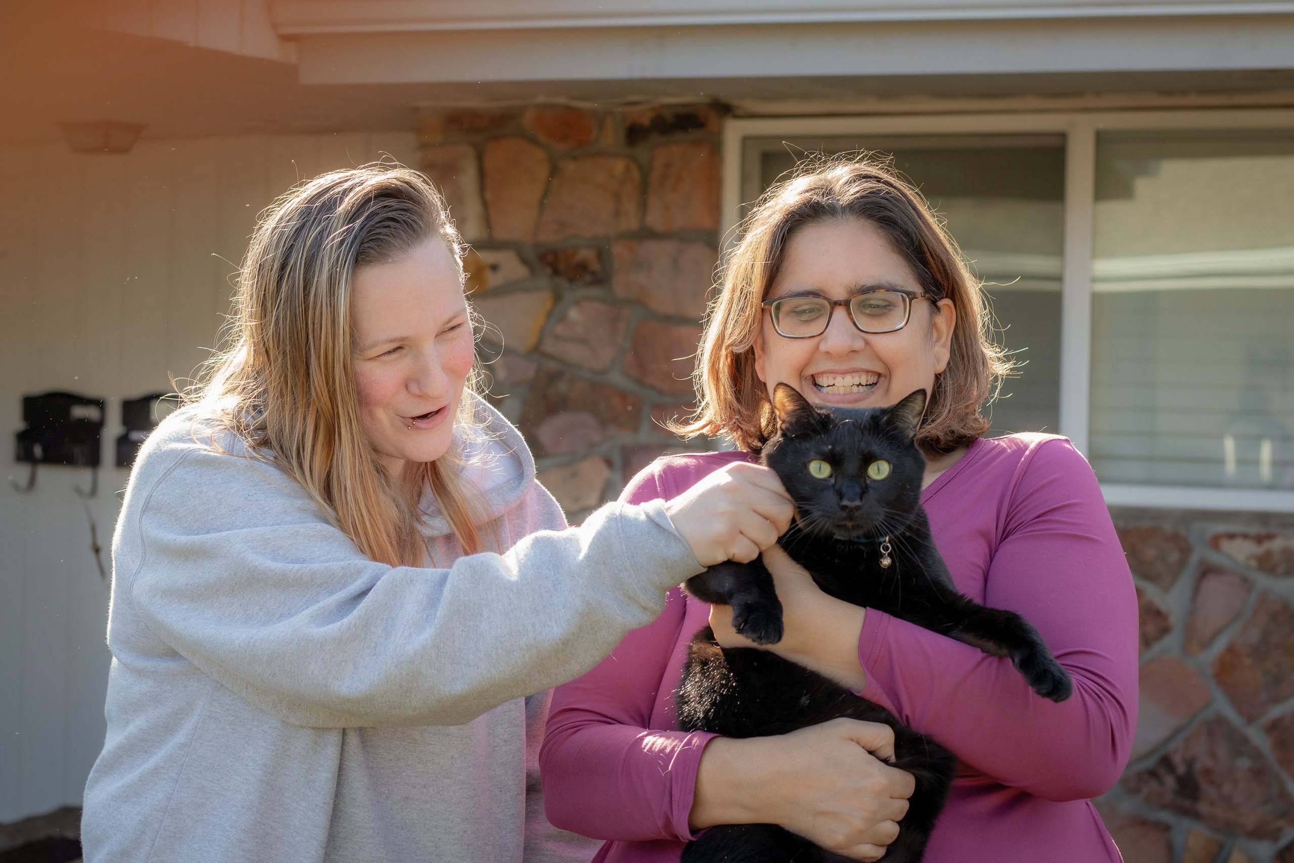 MVa Volunteers and woman with disabilities holding a cat and smiling outside residential housing